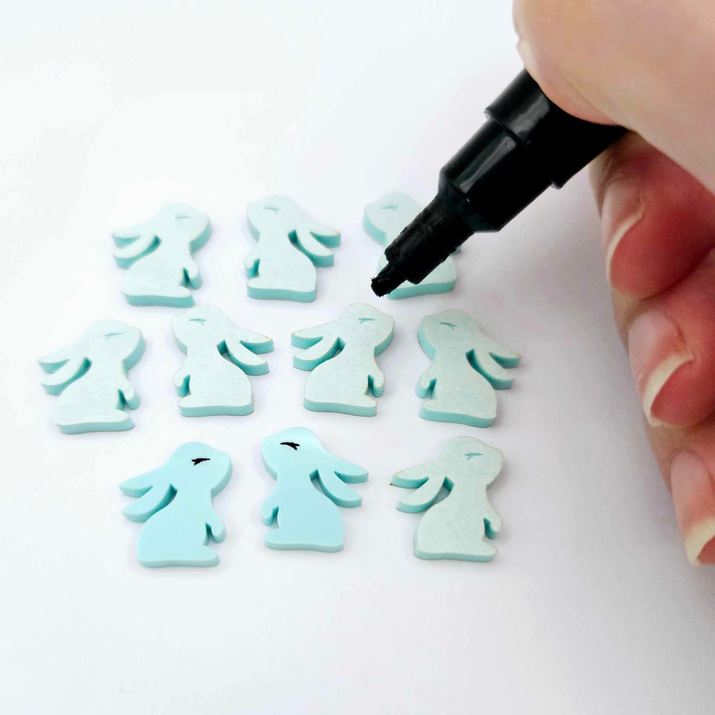 Pastel aqua bunny stud blanks showing finished paint filled black eyelashes on two studs, with the rest shown as supplied with protective film