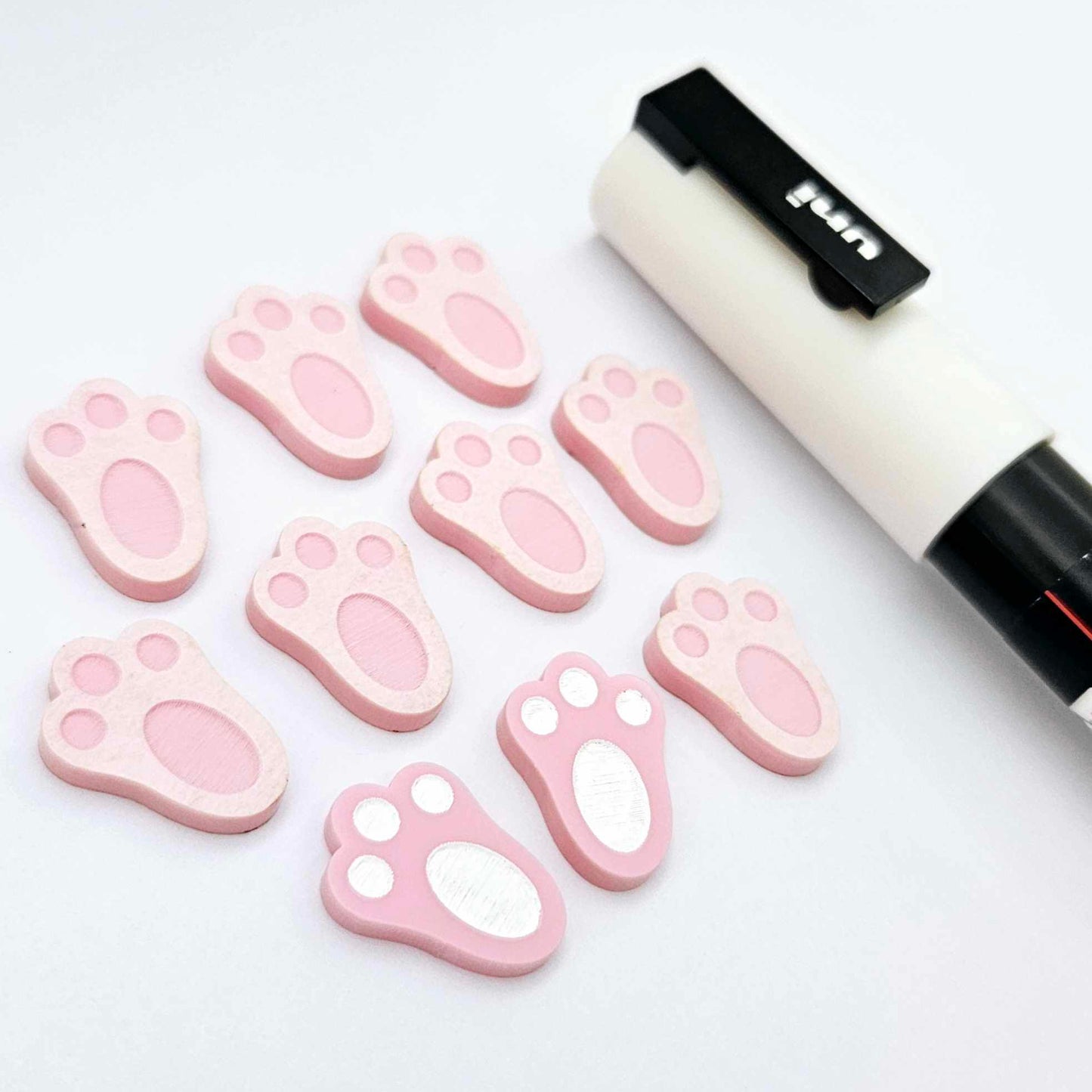 Pastel pink bunny paw print stud blanks showing two paint filled white and several unpainted pieces, with a white Posca paint pen included in the image