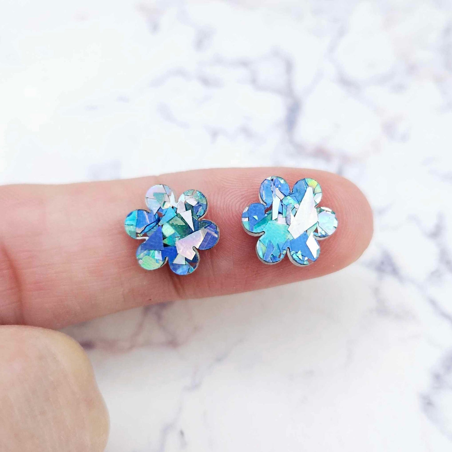 Two 10mm glitter flower stud blanks in Chunky Aqua colour, shown on a finger for size reference