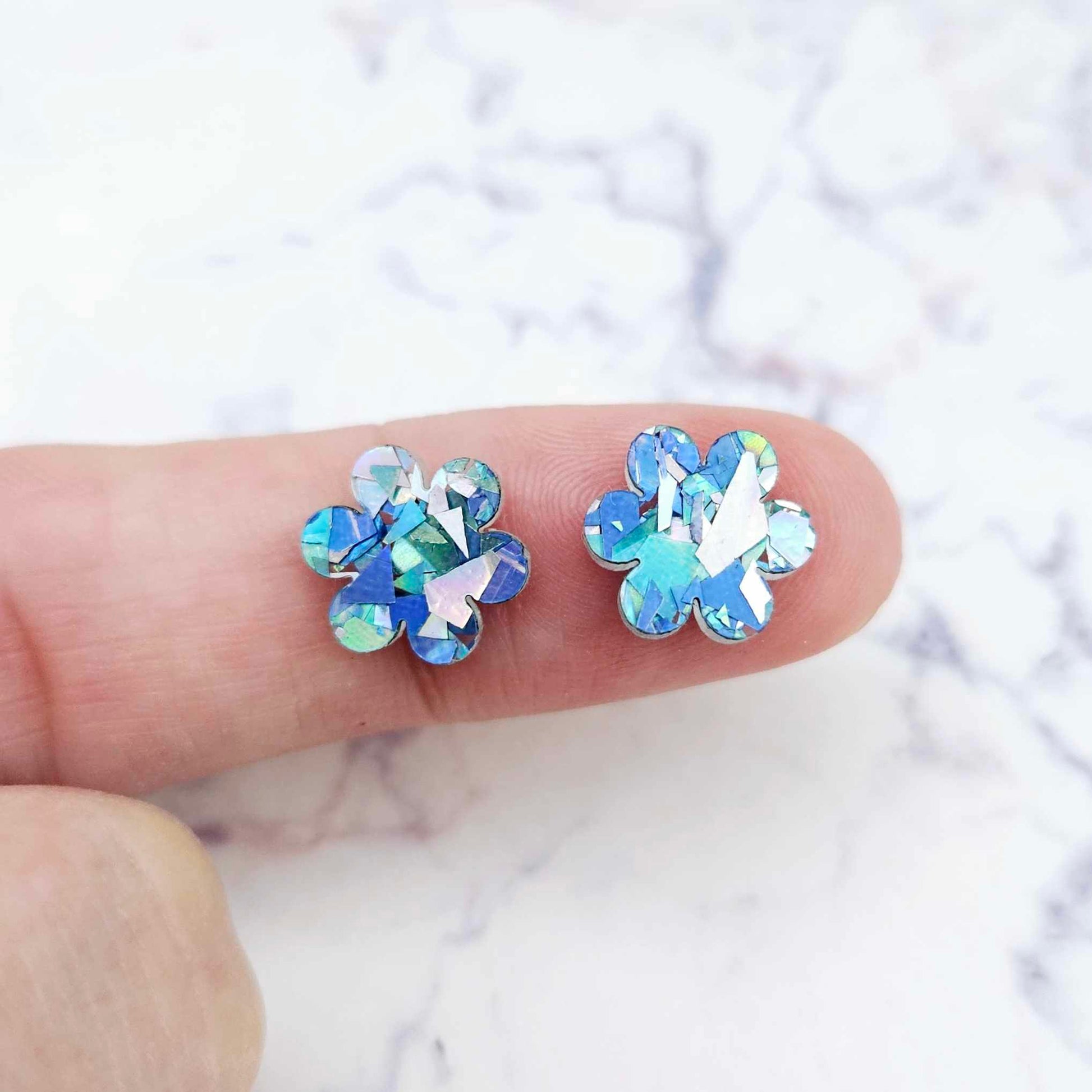 Two 10mm glitter flower stud blanks in Chunky Aqua colour, shown on a finger for size reference