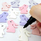 32mm pastel pink, pastel purple and white bunny dangle blanks mixed pack showing paint filled black eyelashes, with remaining pieces shown with protective paper as supplied