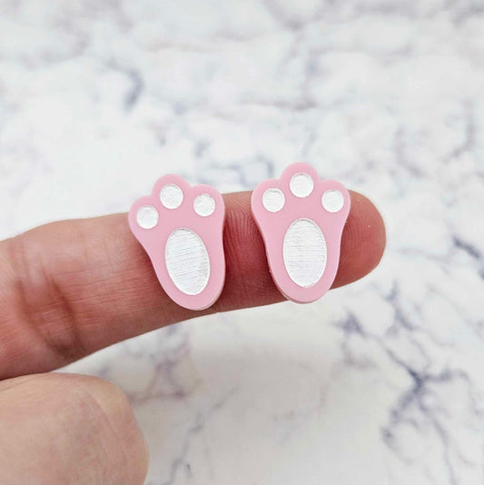 Close-up of two pastel pink acrylic bunny paw print stud blanks with engraved pads paint filled white