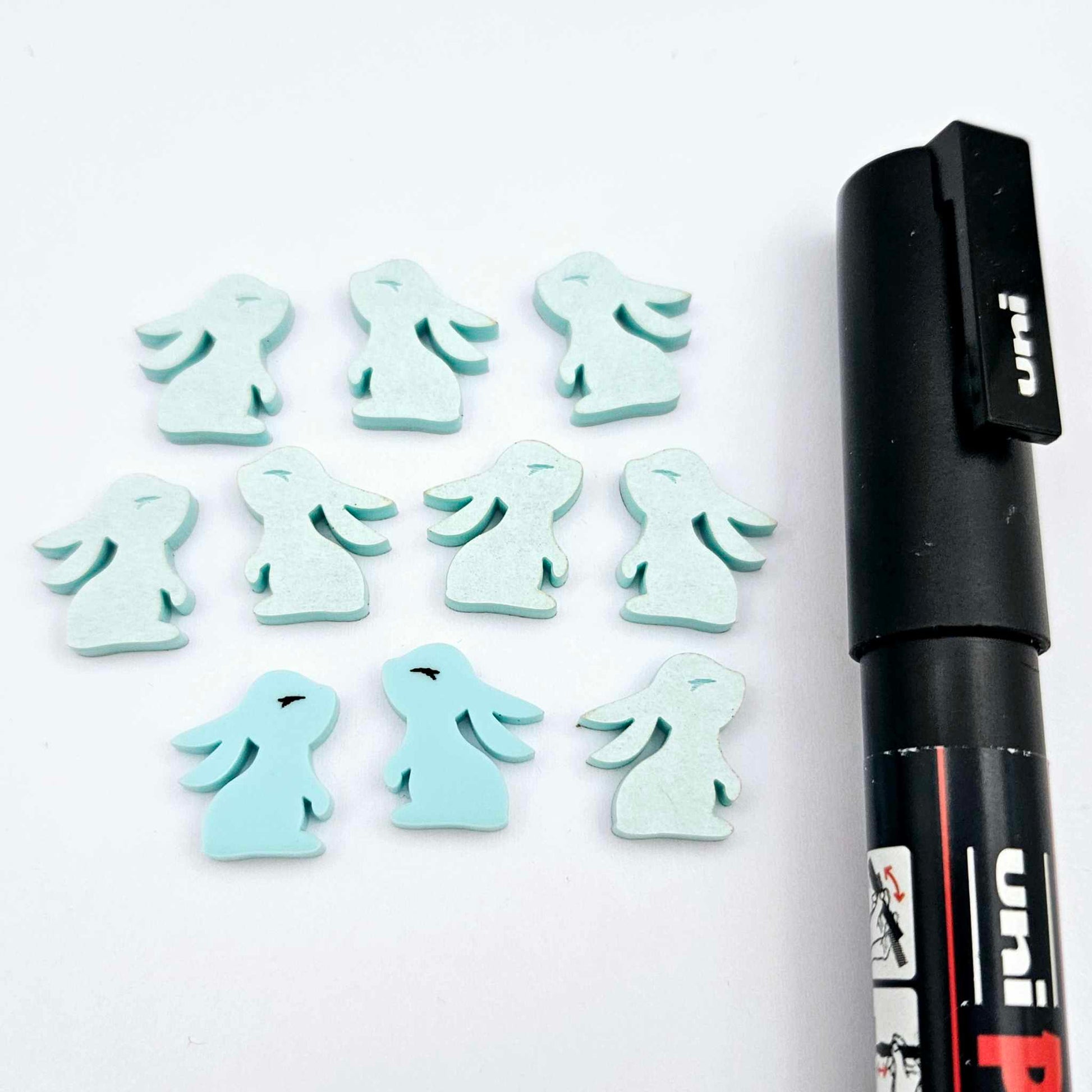 Pastel aqua bunny stud blanks showing finished paint filled black eyelashes on two studs, with the rest shown as supplied with protective film