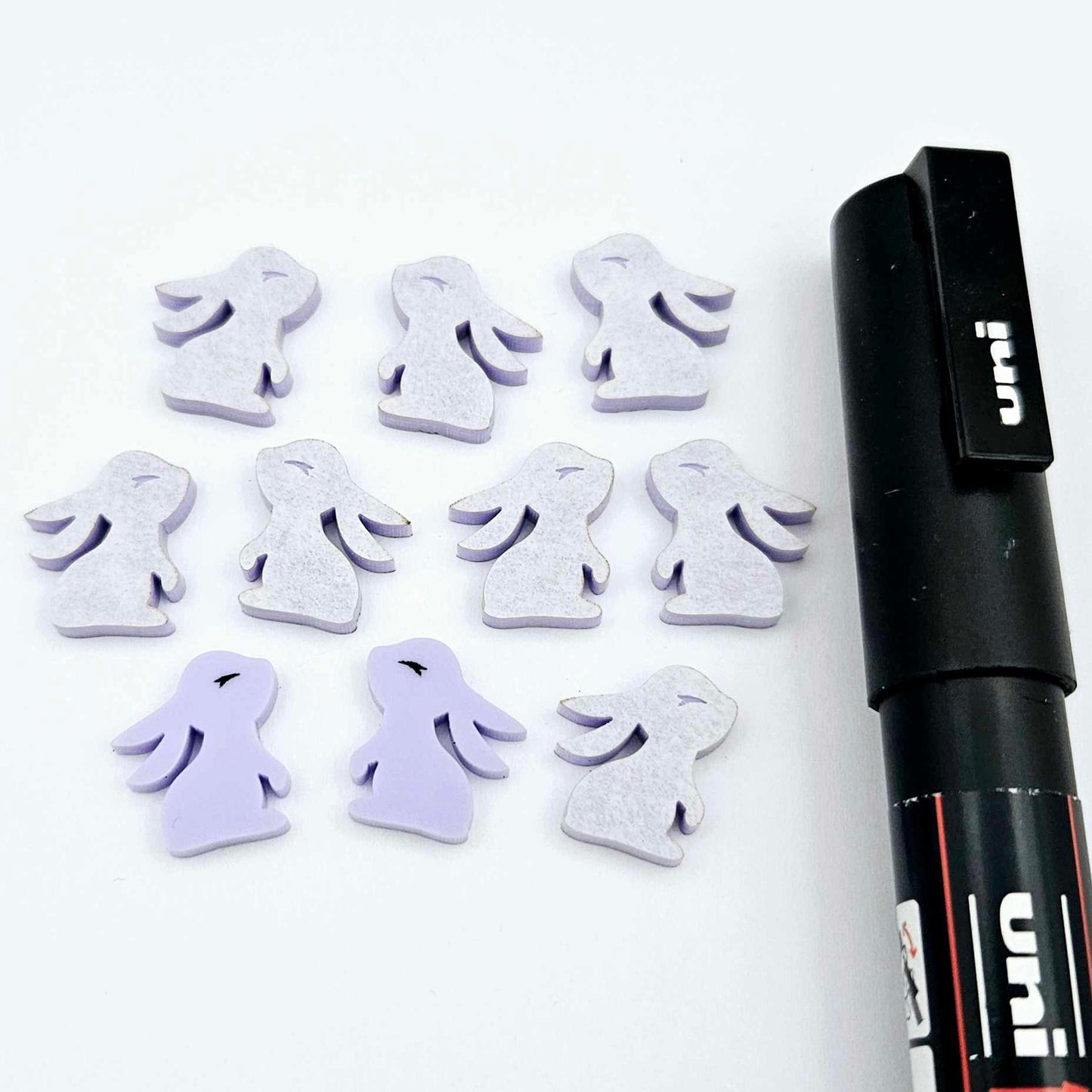 Pastel purple bunny stud blanks showing finished paint filled black eyelashes on two studs, with the rest shown as supplied with protective film