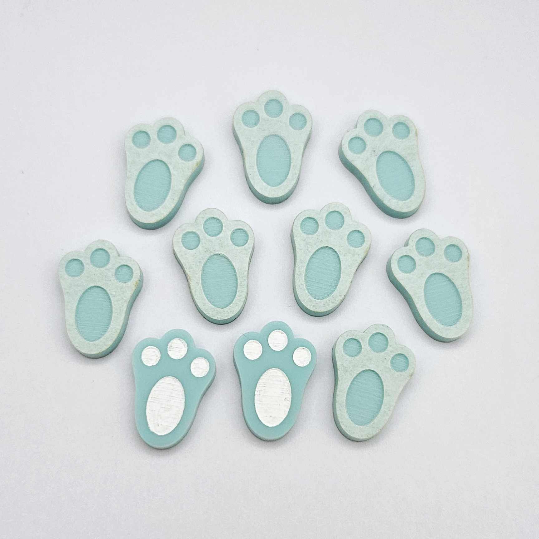 Pastel aqua bunny paw print stud blanks showing two paint filled white and several unpainted pieces