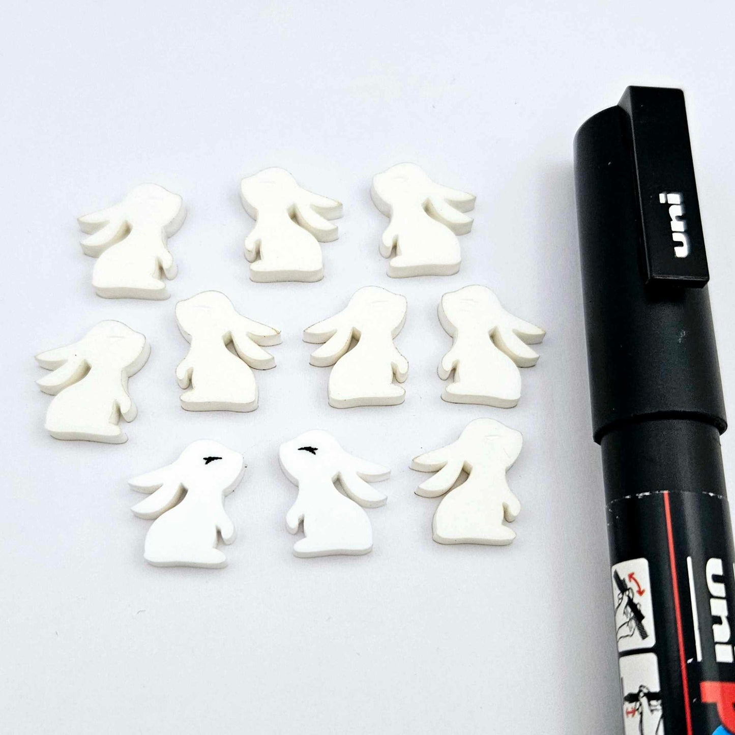 white acrylic bunny stud blanks showing finished paint filled black eyelashes on two studs, with the rest shown as supplied with protective film