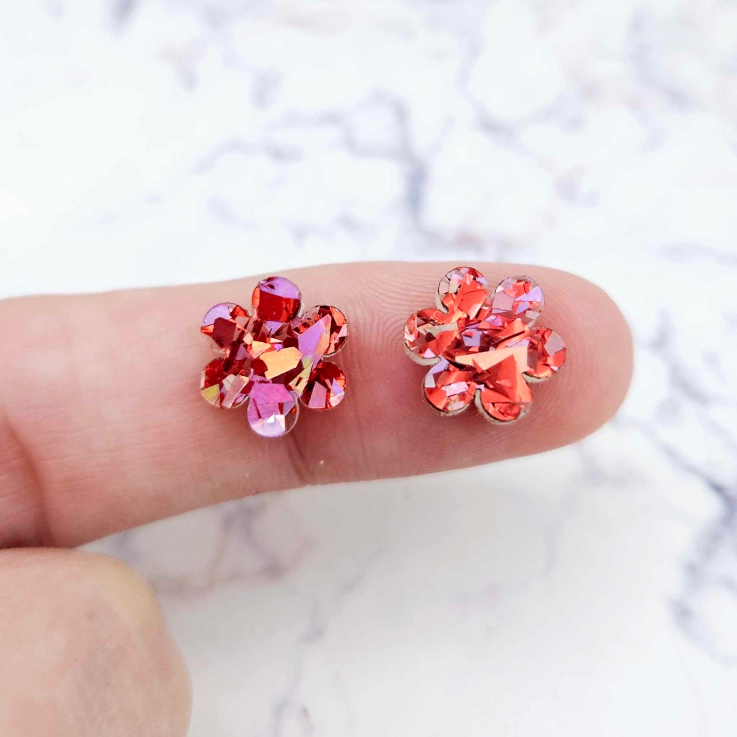 Two 10mm glitter flower stud blanks in Chunky Love colour, shown on a finger for size reference