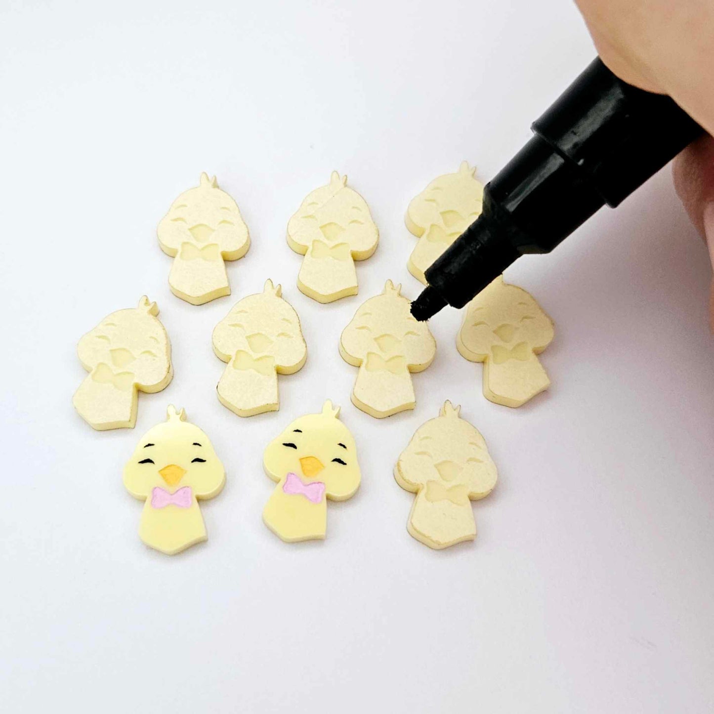 Pastel yellow acrylic chicken head stud blanks showing two paint filled examples and several unpainted pieces, with Posca paint pens included in the image