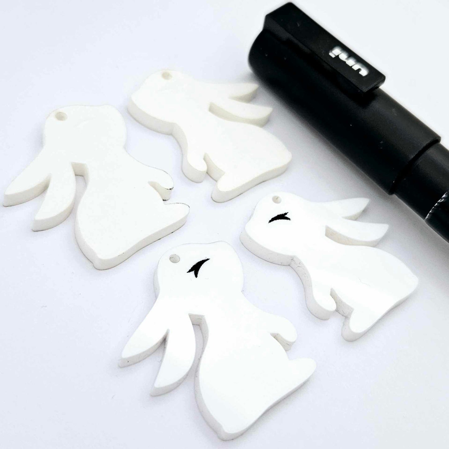 32mm white bunny dangle blanks showing paint filled black eyelashes on two pieces, with remaining pieces shown with protective paper as supplied