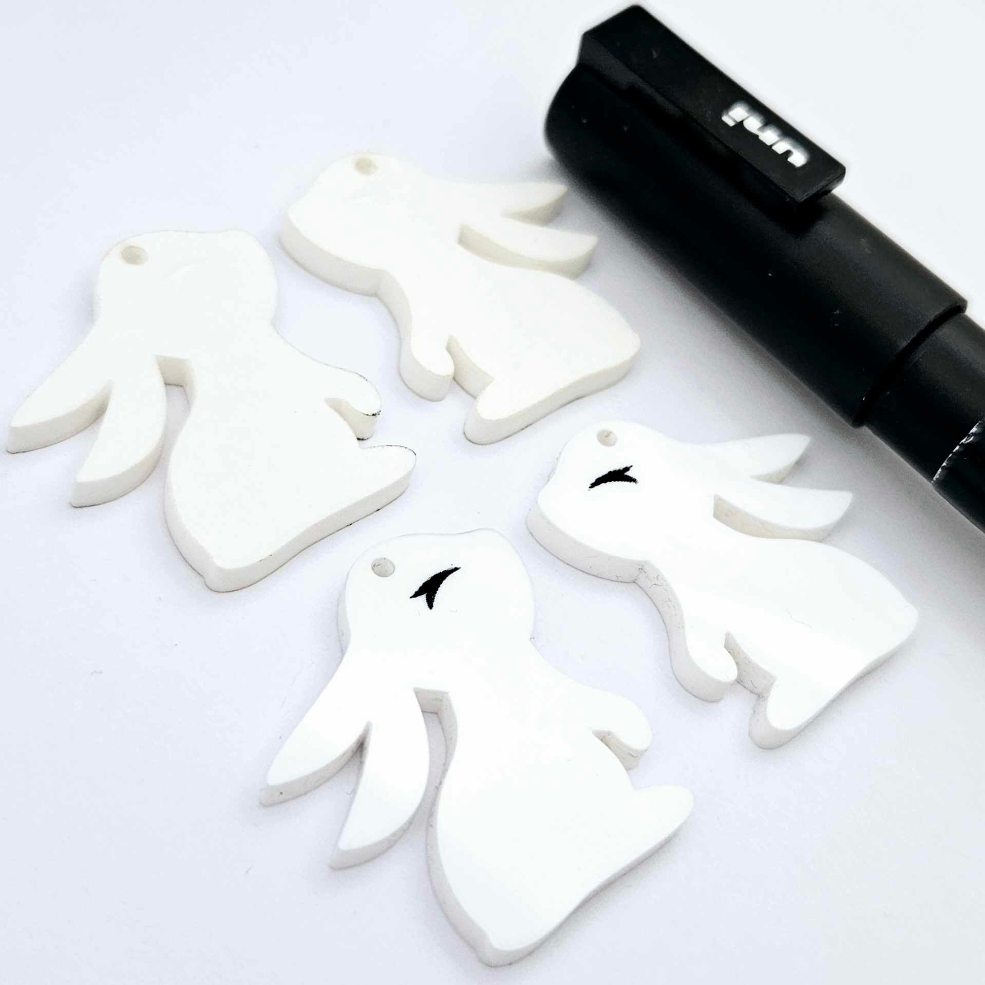 32mm white bunny dangle blanks showing paint filled black eyelashes on two pieces, with remaining pieces shown with protective paper as supplied