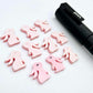 Pastel pink bunny stud blanks showing finished paint filled black eyelashes on two studs, with the rest shown as supplied with protective film