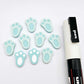 Pastel aqua bunny paw print stud blanks showing two paint filled white and several unpainted pieces, with a white Posca paint pen included in the image