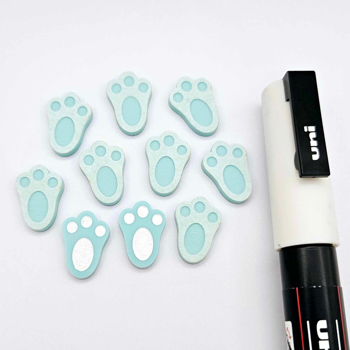 Pastel aqua bunny paw print stud blanks showing two paint filled white and several unpainted pieces, with a white Posca paint pen included in the image