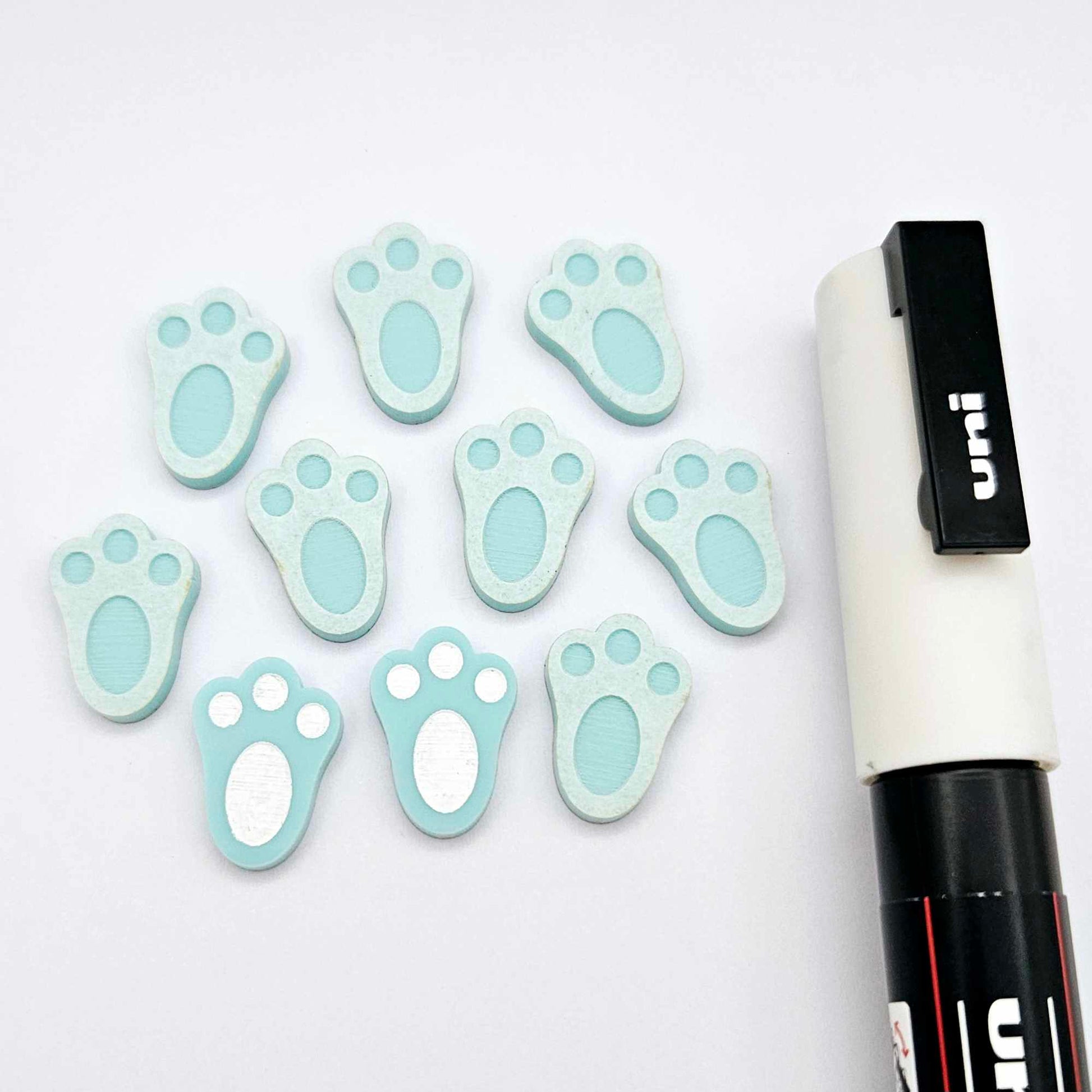 Pastel aqua bunny paw print stud blanks showing two paint filled white and several unpainted pieces, with a white Posca paint pen included in the image