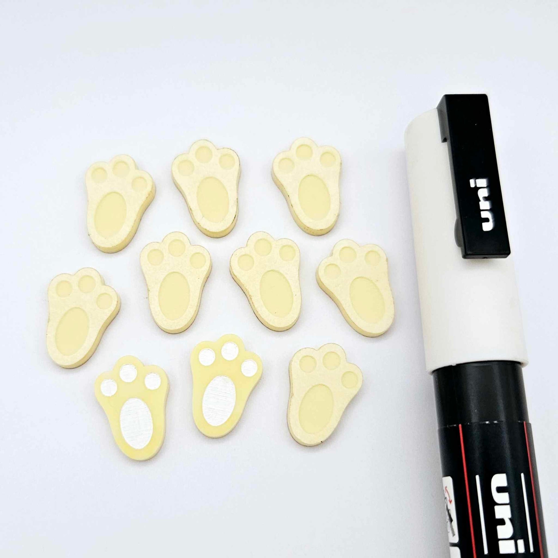 Pastel yellow bunny paw print stud blanks showing two paint filled white and several unpainted pieces, with a white Posca paint pen included in the image