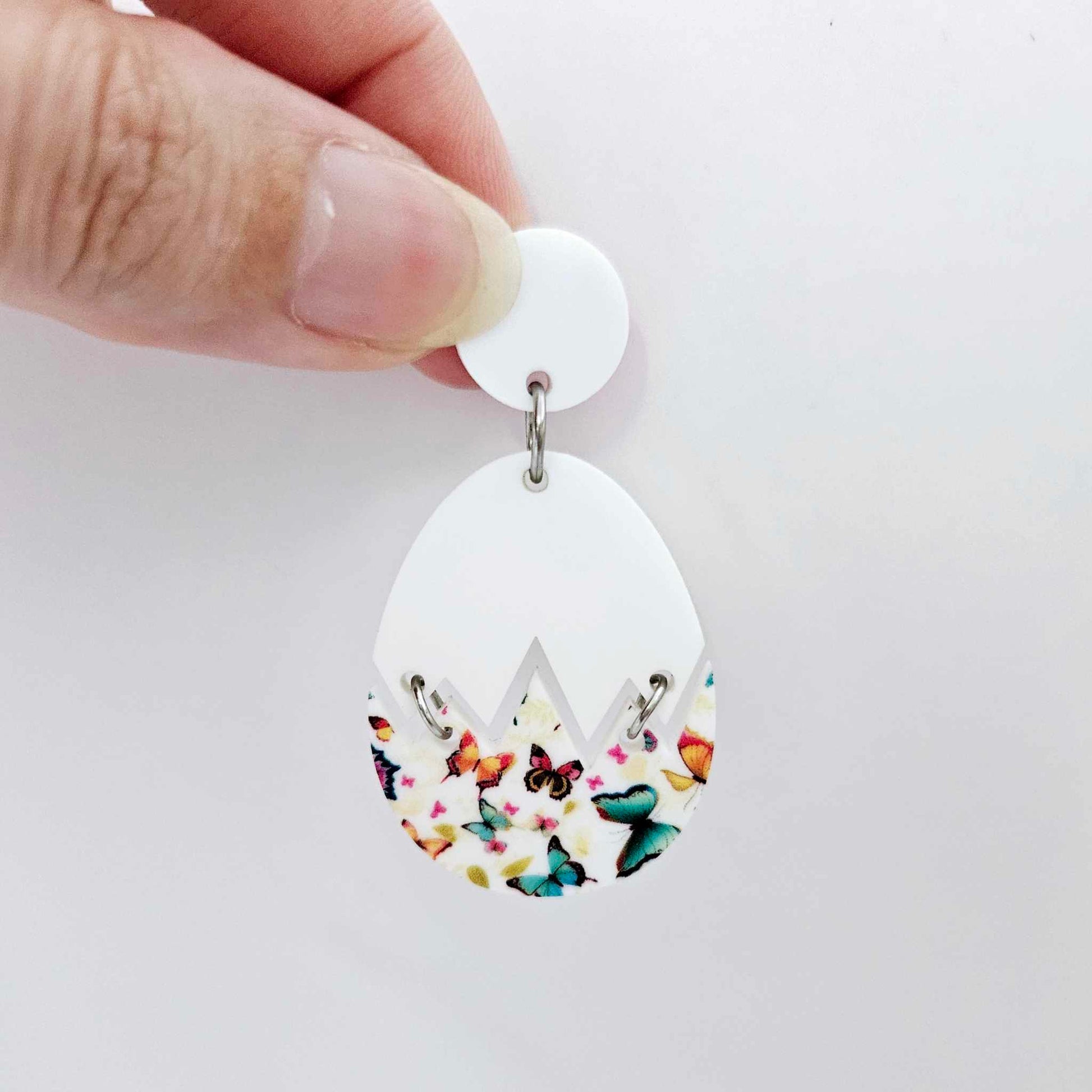 Assembled cracked egg acrylic dangle earring blank with white top and butterfly UV printed bottom, hanging from a 14mm white earring topper