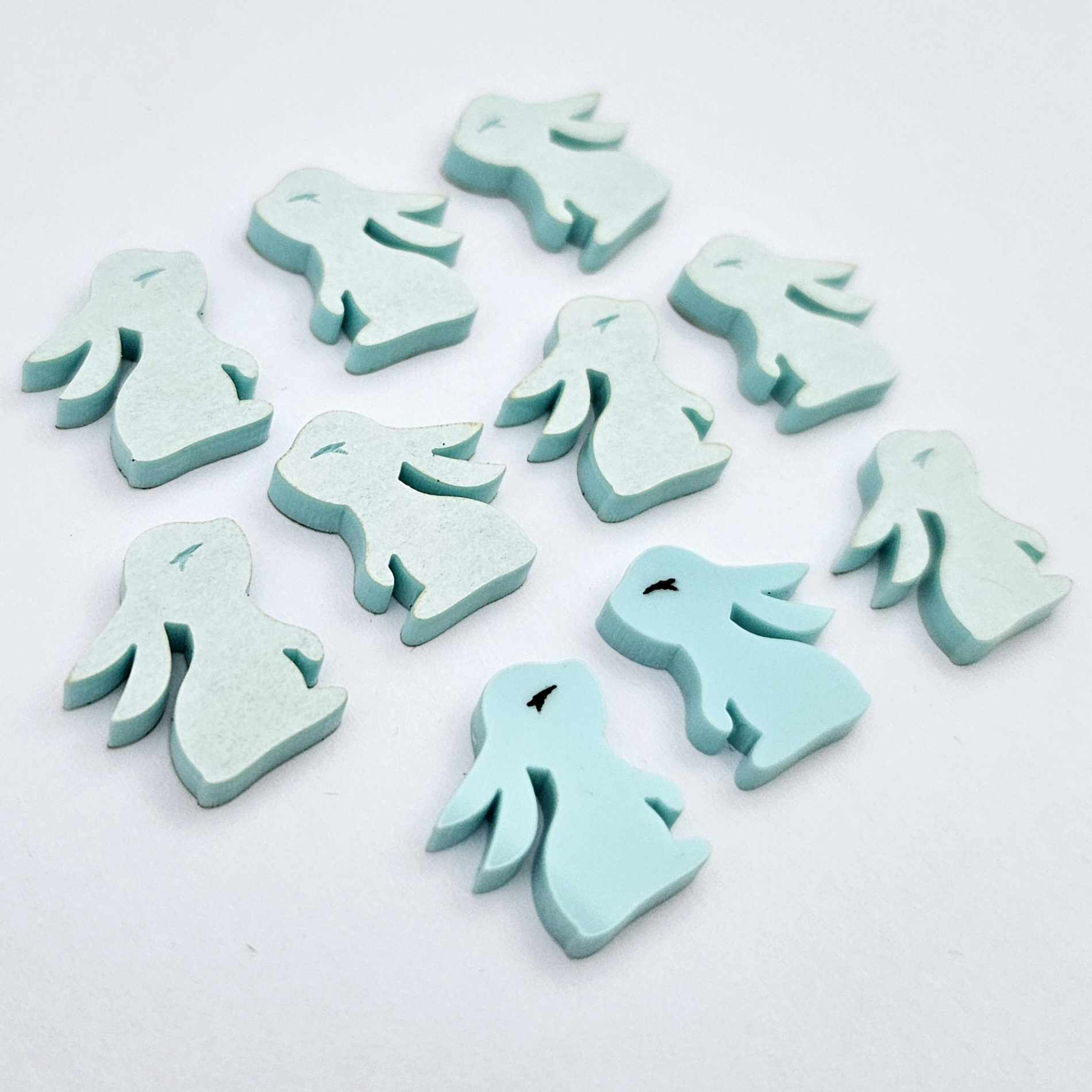 Pastel aqua bunny stud blanks showing finished paint filled black eyelashes on two studs, with the rest shown as supplied with protective film