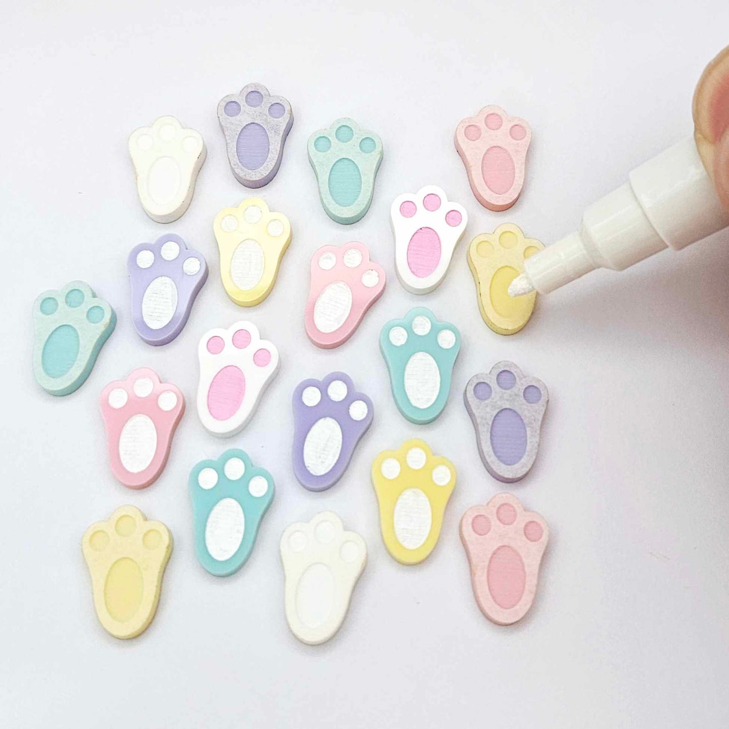 white and pastel bunny paw print stud blanks showing some paint filled and several unpainted pieces, with a Light Pink and White Posca paint pen included in the image