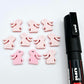 Pastel pink bunny stud blanks showing finished paint filled black eyelashes on two studs, with the rest shown as supplied with protective film