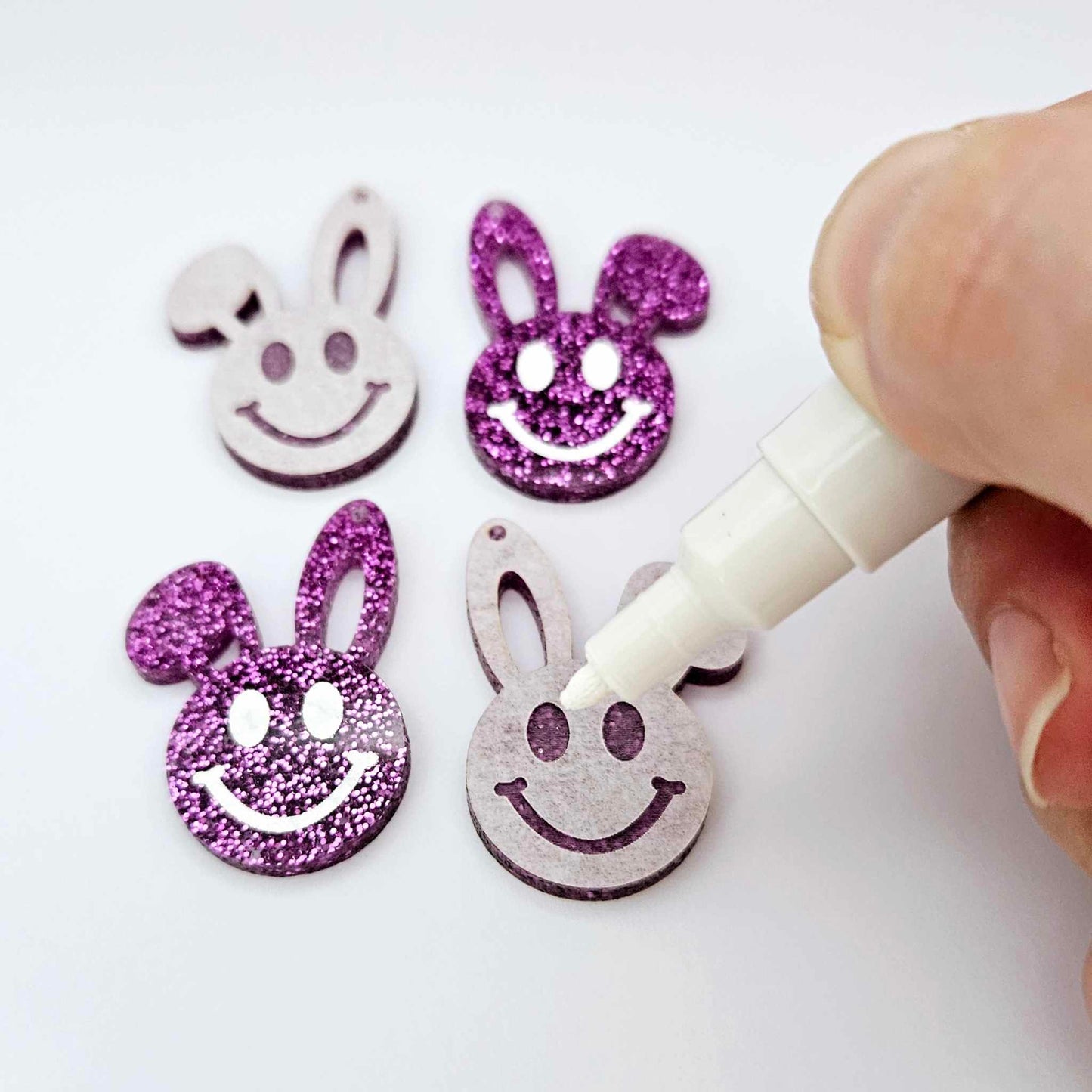 38mm purple glitter acrylic bunny dangle blanks with engraved smiley face, two paint filled white and two others unfilled with protective film on, shown with a White Posca paint pen