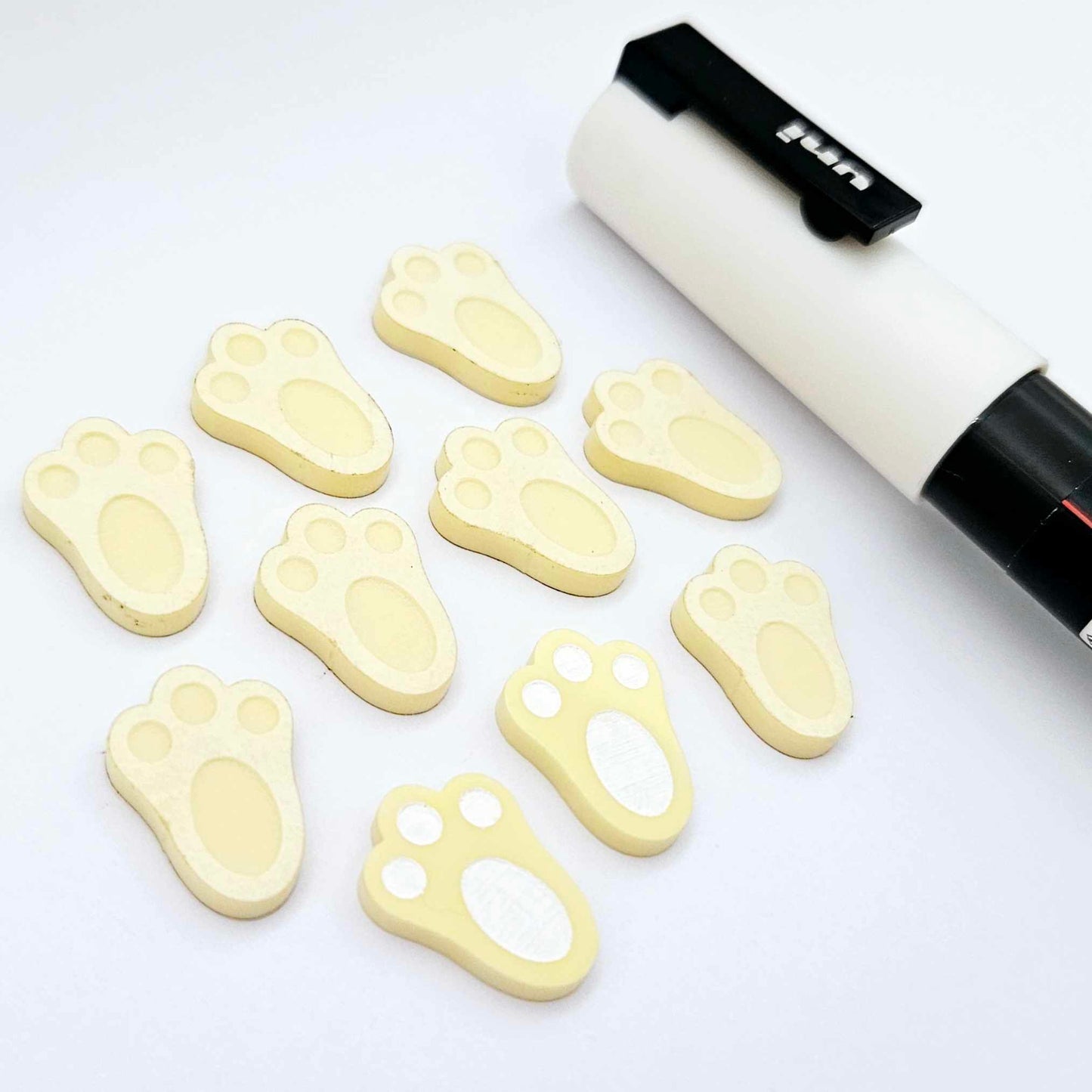 Pastel yellow bunny paw print stud blanks showing two paint filled white and several unpainted pieces, with a white Posca paint pen included in the image