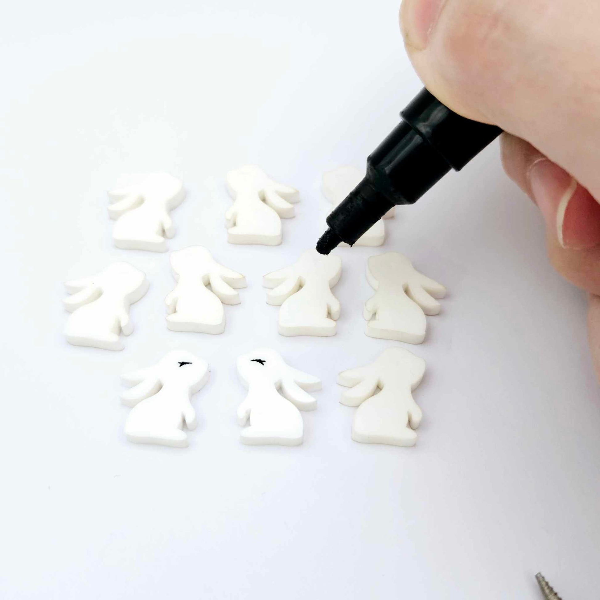 white acrylic bunny stud blanks showing finished paint filled black eyelashes on two studs, with the rest shown as supplied with protective film