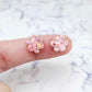 Two 10mm glitter flower stud blanks in Chunky Holographic Rose Gold colour, shown on a finger for size reference