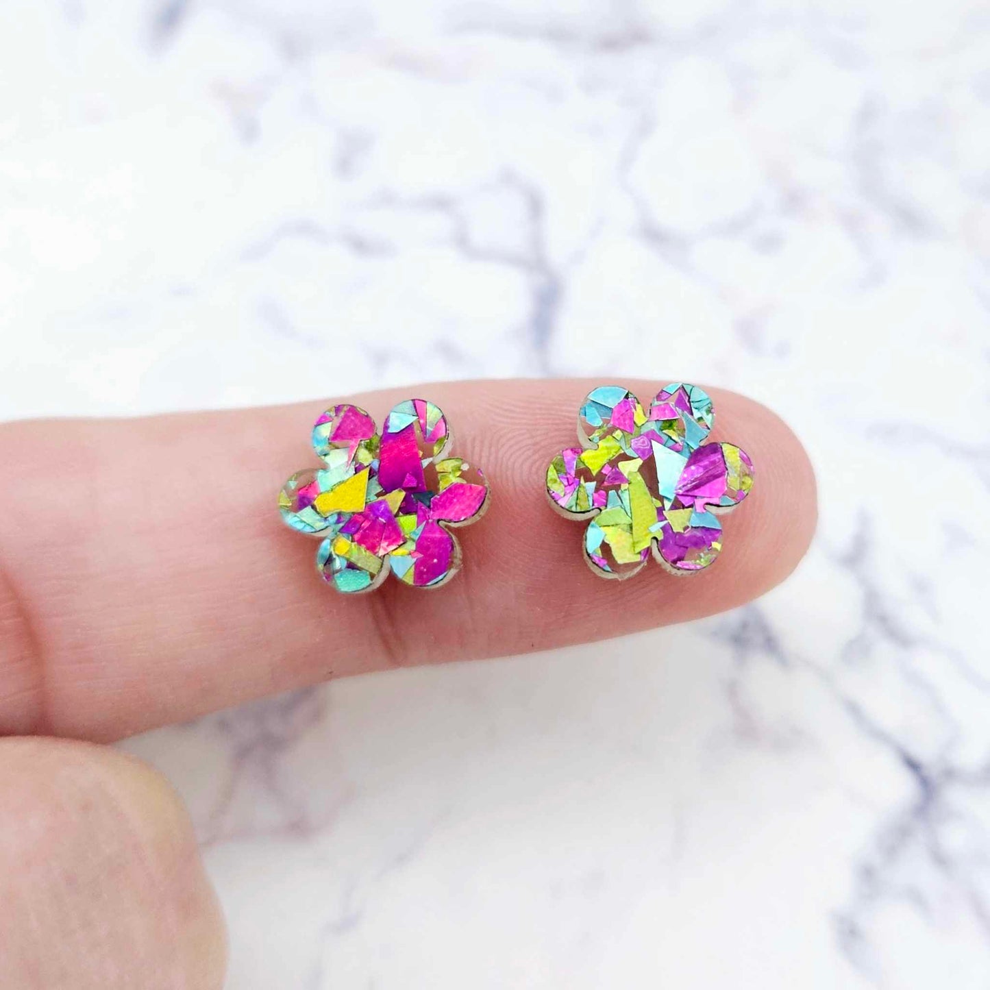 Two 10mm glitter flower stud blanks in Chunky Peacock colour, shown on a finger for size reference
