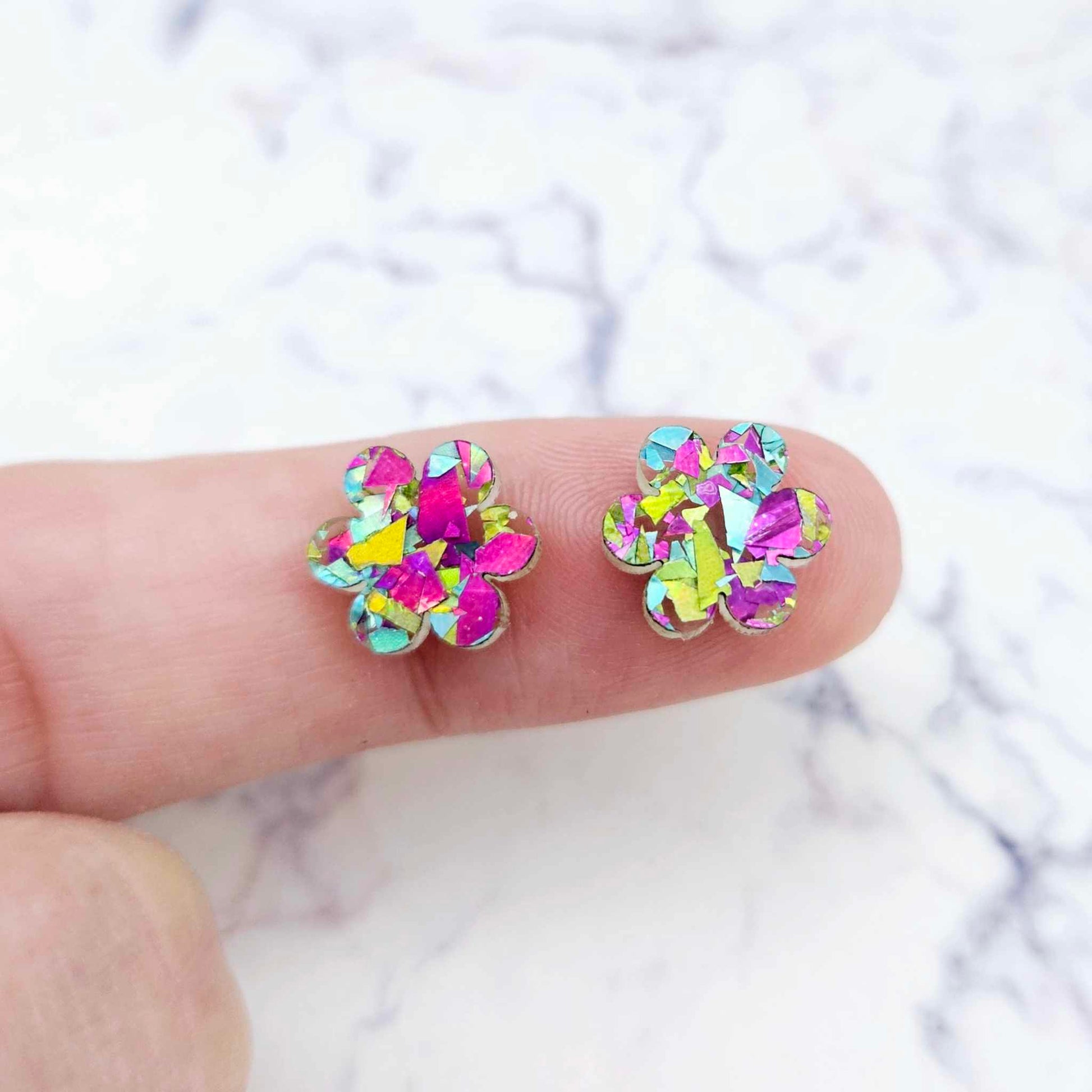 Two 10mm glitter flower stud blanks in Chunky Peacock colour, shown on a finger for size reference