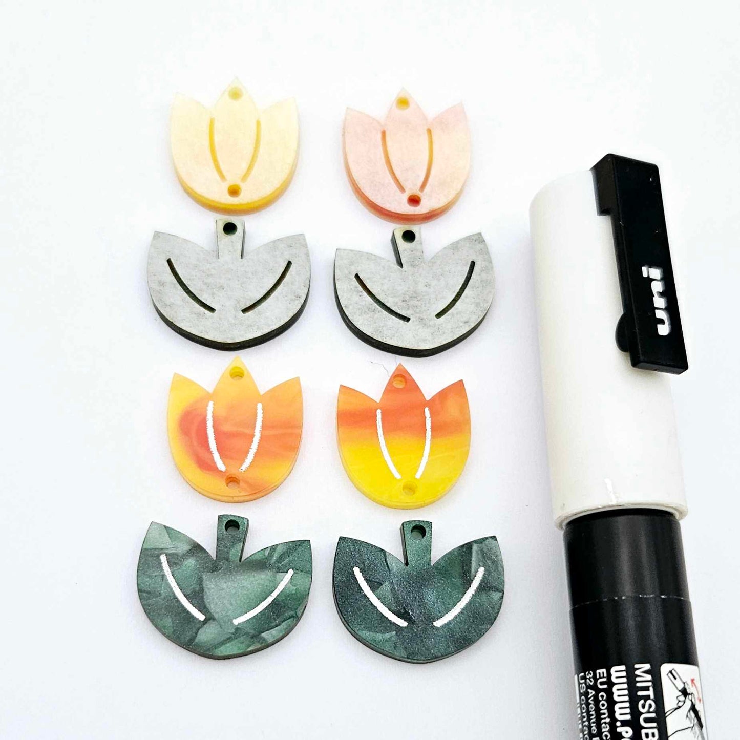 Two-piece tulip acrylic dangle blanks in orange artist swirl and green mineral acrylic, paint filled white on one pair with remaining pair unfilled, shown with a white Posca paint pen