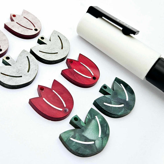 Two-piece tulip acrylic dangle blanks in red marble and green mineral acrylic, paint filled white on one pair with remaining pair unfilled, shown with a white Posca paint pen