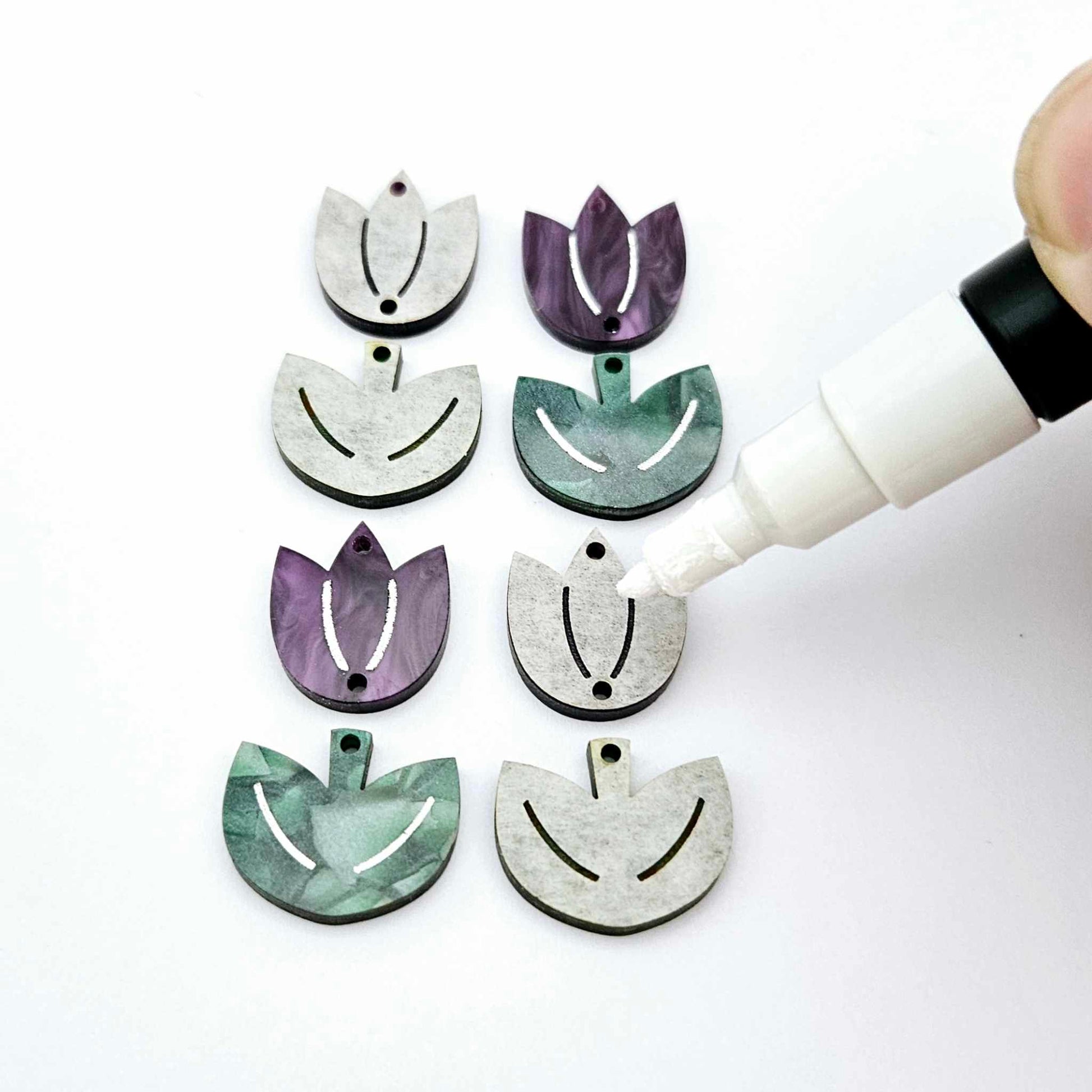 Two-piece tulip acrylic dangle blanks in purple marble and green mineral acrylic, paint filled white on one pair with remaining pair unfilled, shown with a white Posca paint pen