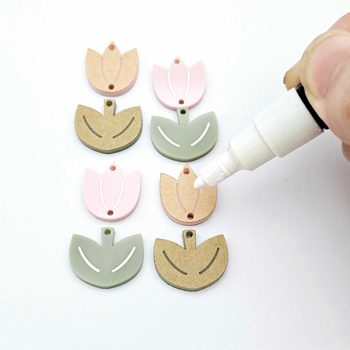 Two-piece tulip acrylic dangle blanks in dusty pale pink and olive green, paint filled white on one pair with remaining pair unfilled, shown with a white Posca paint pen