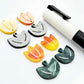 Two-piece tulip acrylic dangle blanks in orange artist swirl and green mineral acrylic, paint filled white on one pair with remaining pair unfilled, shown with a white Posca paint pen