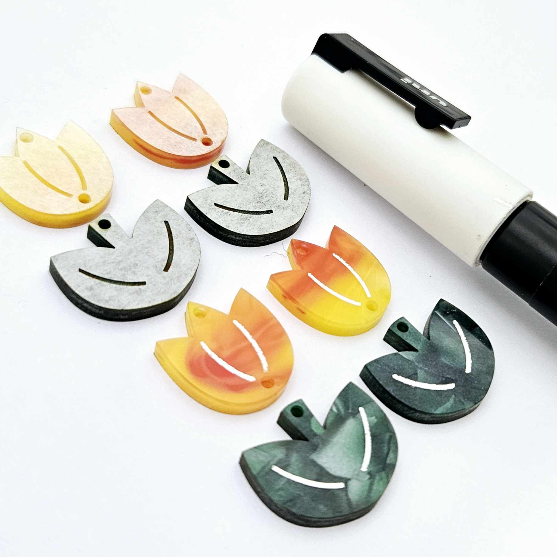 Two-piece tulip acrylic dangle blanks in orange artist swirl and green mineral acrylic, paint filled white on one pair with remaining pair unfilled, shown with a white Posca paint pen