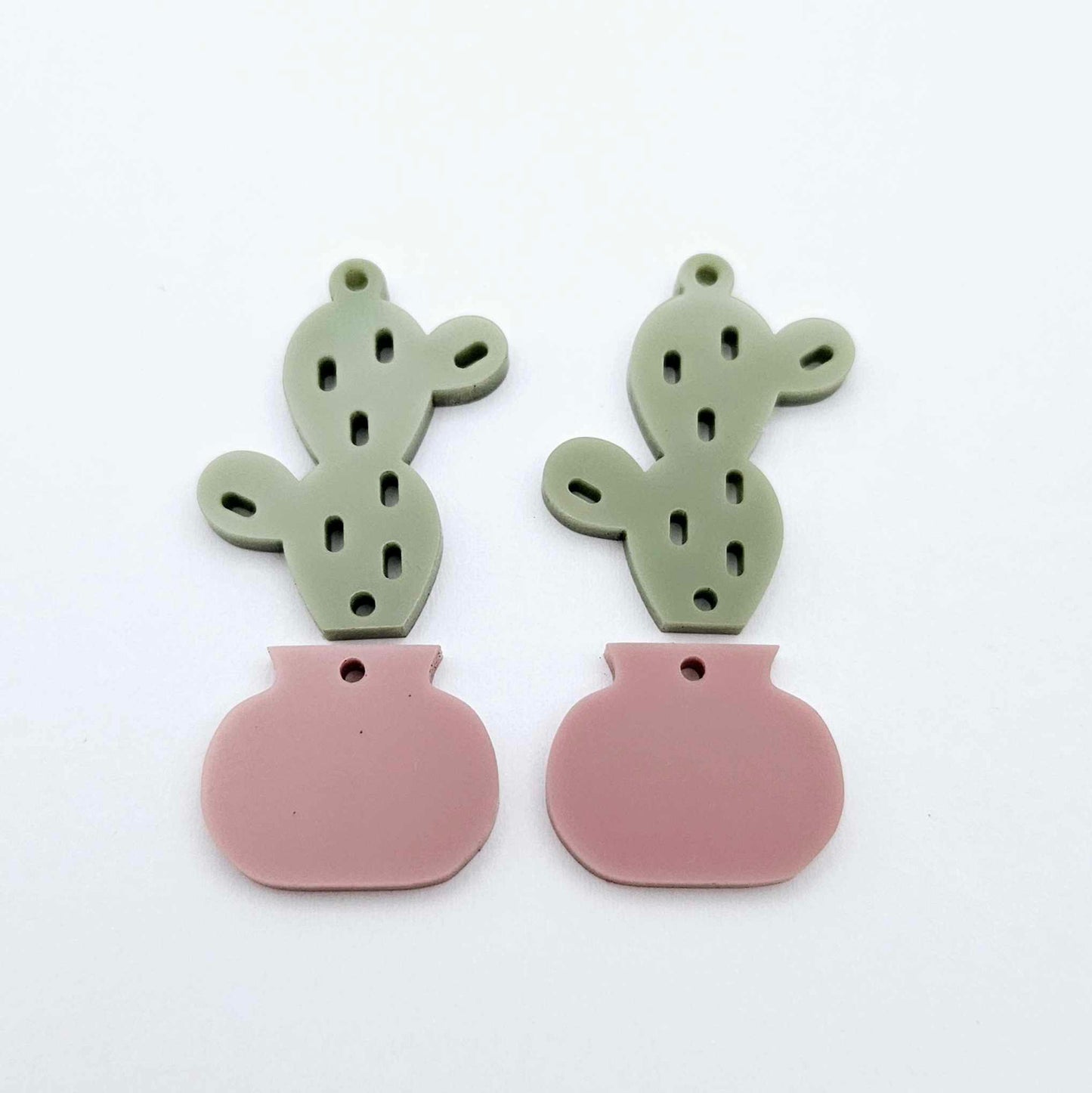 Two-piece acrylic cactus dangle blanks in olive green and dusty rose pink, shown unassembled with cactus top and pot bottom pieces laid flat