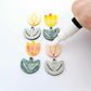 Two-piece tulip acrylic dangle blanks in orange artist swirl and green mineral acrylic, paint filled white on one pair with remaining pair unfilled, shown with a white Posca paint pen