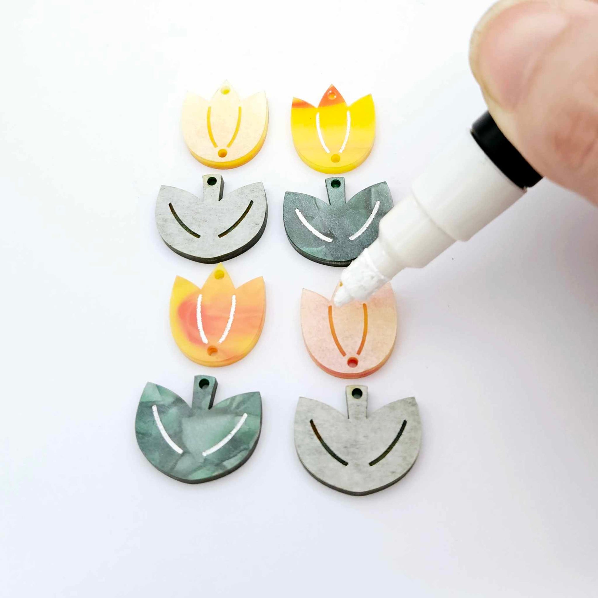 Two-piece tulip acrylic dangle blanks in orange artist swirl and green mineral acrylic, paint filled white on one pair with remaining pair unfilled, shown with a white Posca paint pen
