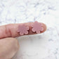 Two 14mm dusty rose pink flower stud blanks, shown on a finger for size reference