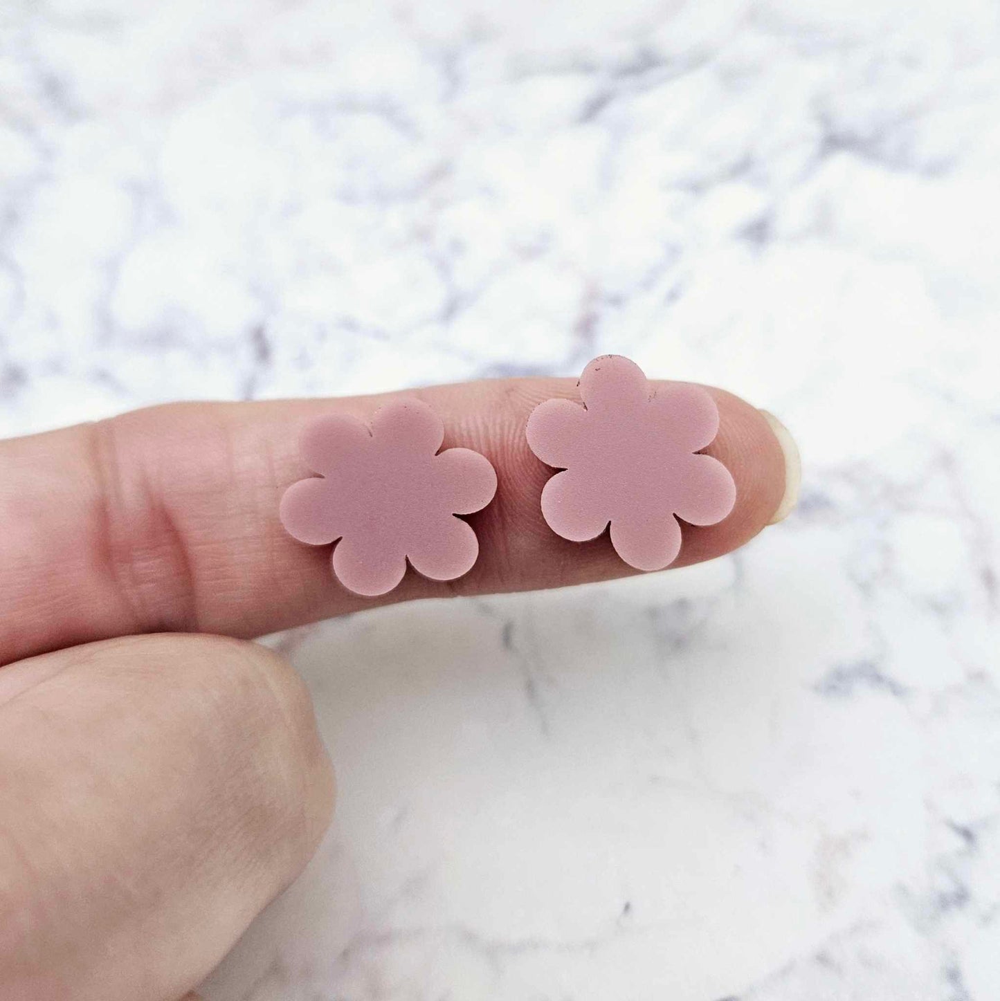 Two 14mm dusty rose pink flower stud blanks, shown on a finger for size reference