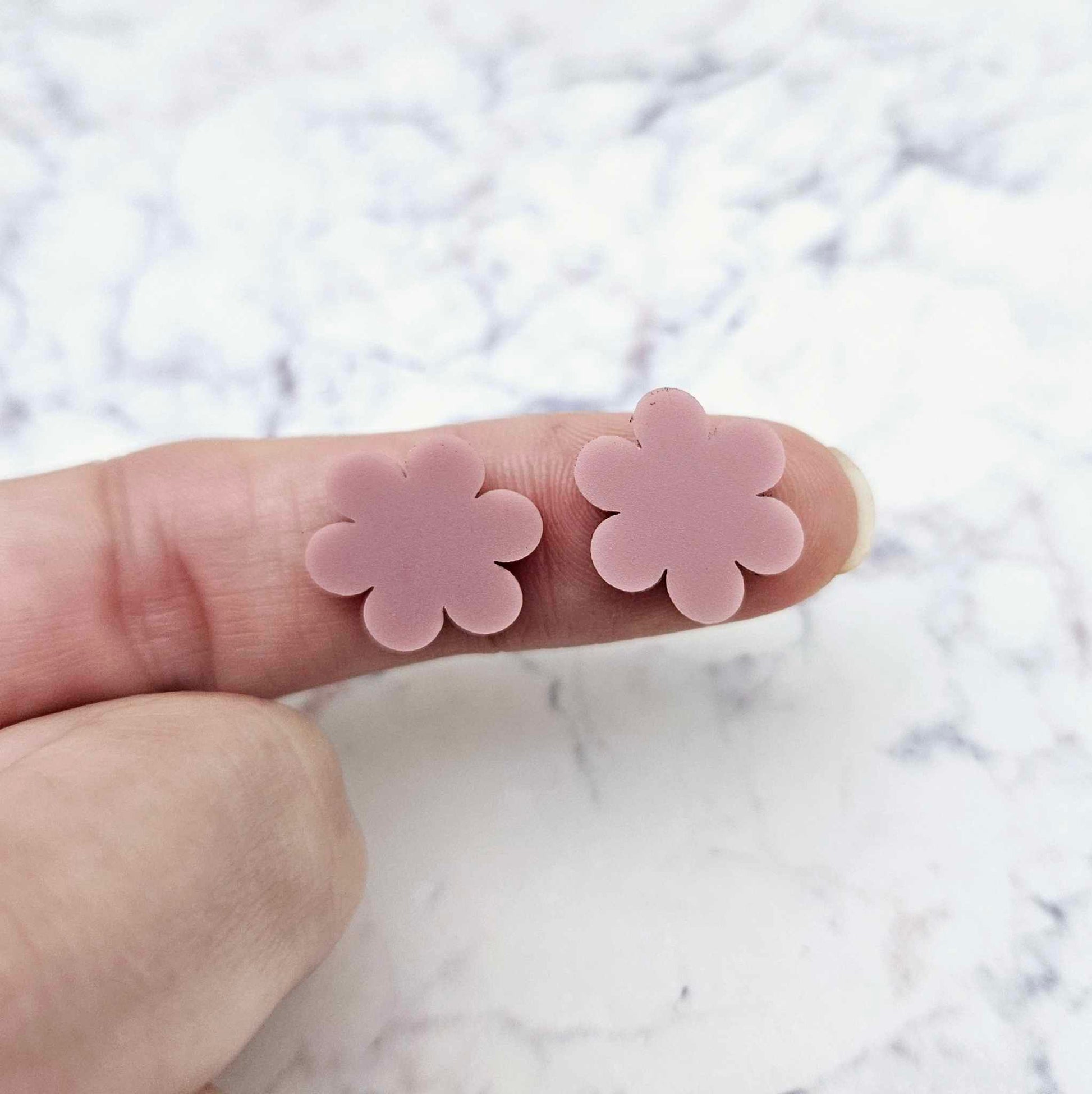 Two 14mm dusty rose pink flower stud blanks, shown on a finger for size reference