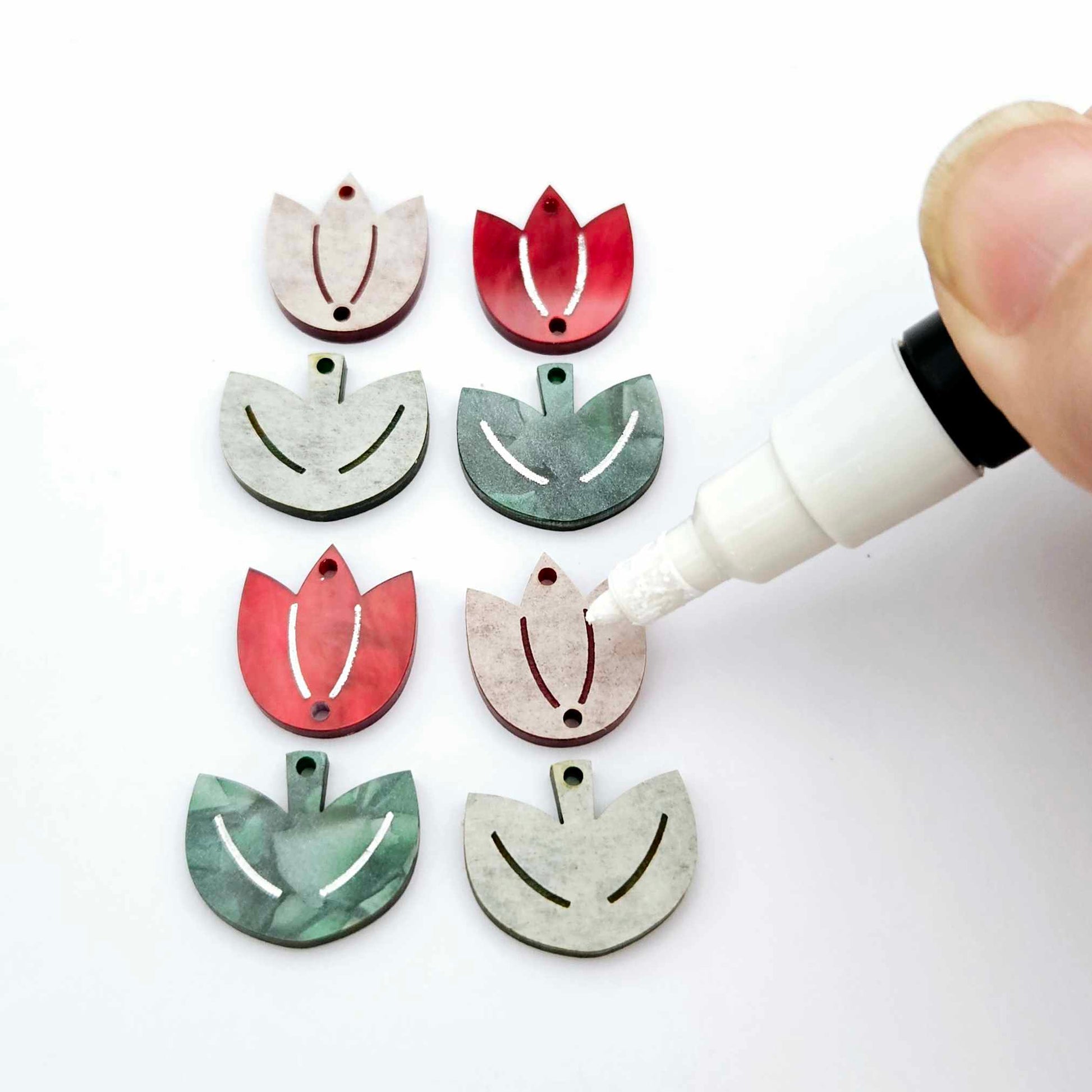 Two-piece tulip acrylic dangle blanks in red marble and green mineral acrylic, paint filled white on one pair with remaining pair unfilled, shown with a white Posca paint pen