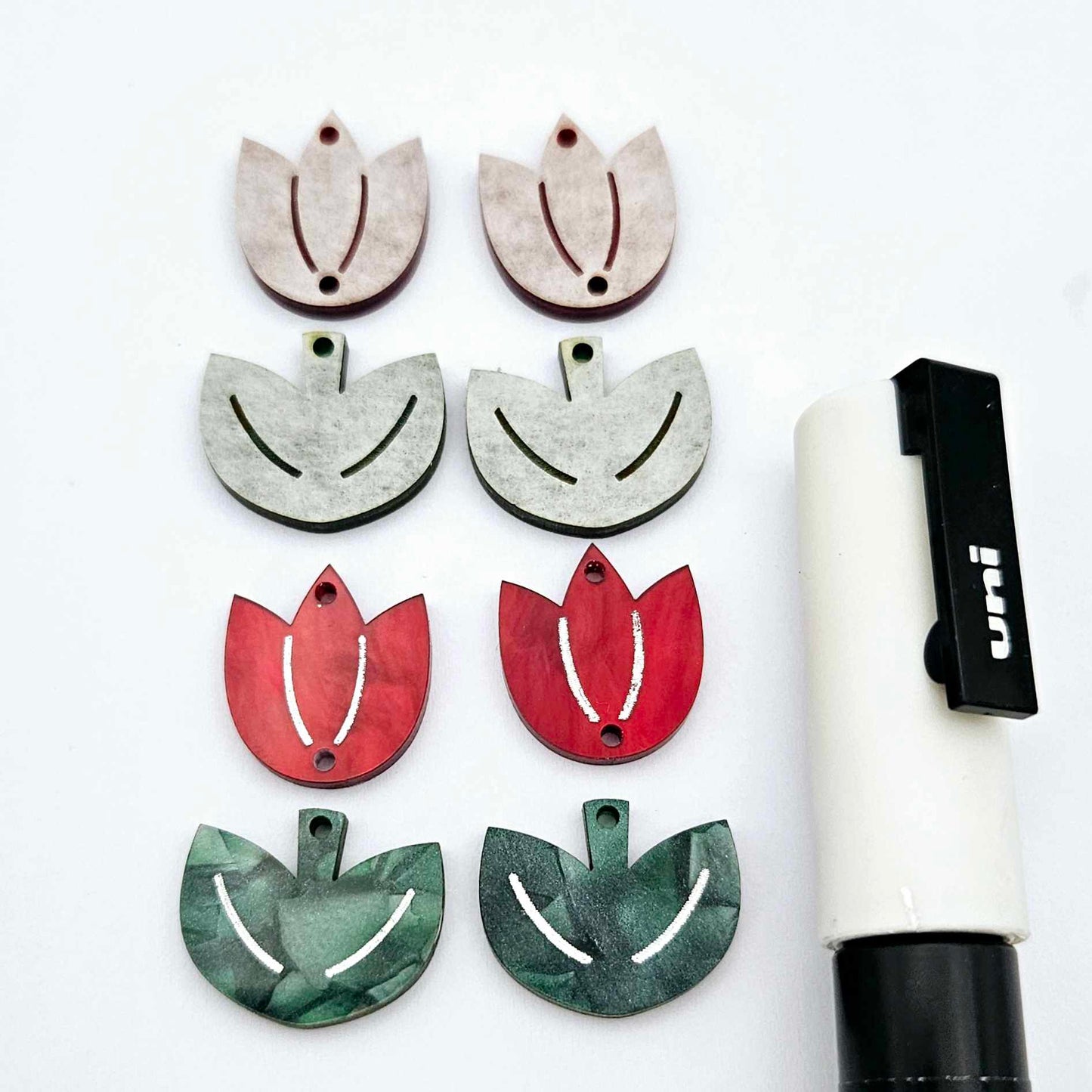 Two-piece tulip acrylic dangle blanks in red marble and green mineral acrylic, paint filled white on one pair with remaining pair unfilled, shown with a white Posca paint pen