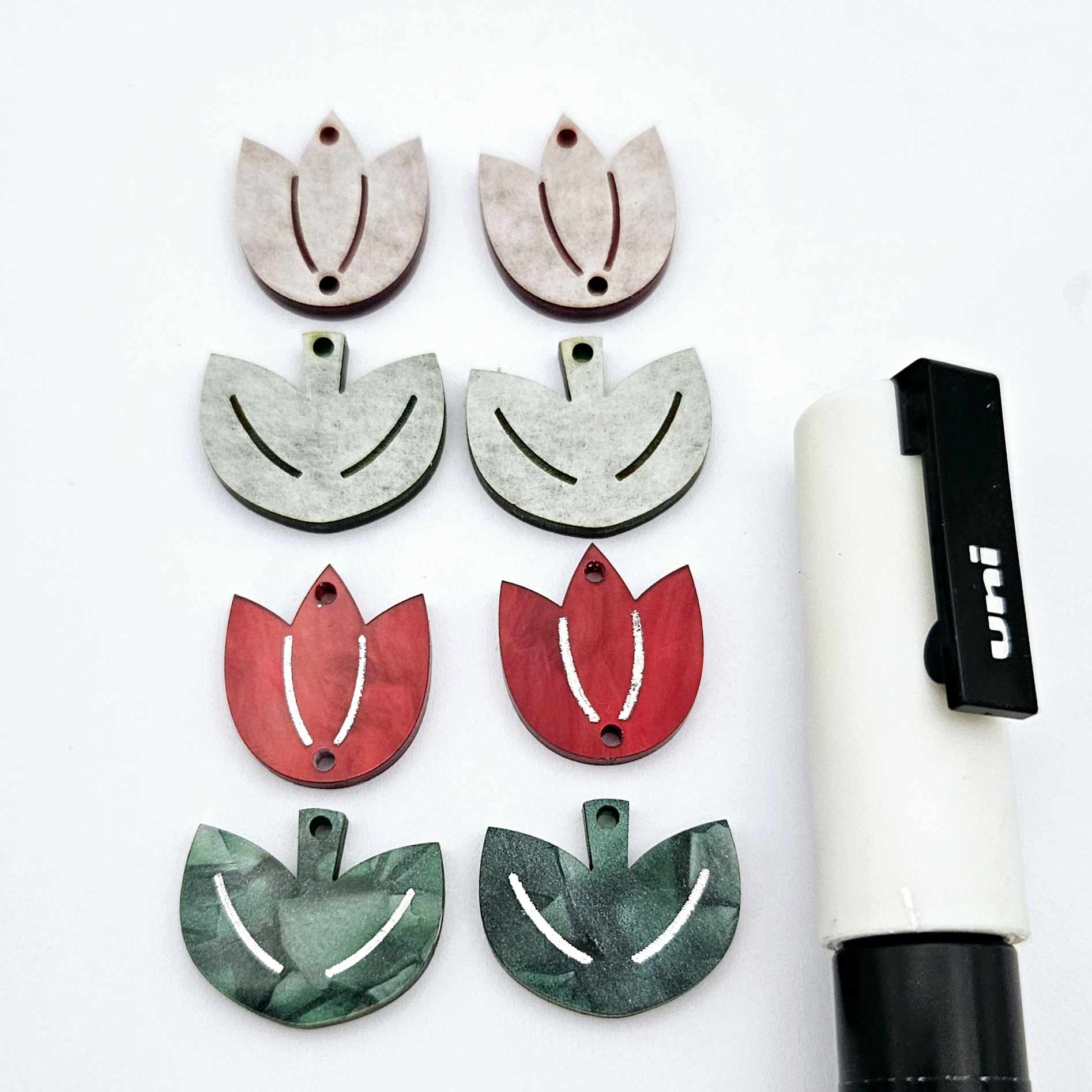 Two-piece tulip acrylic dangle blanks in red marble and green mineral acrylic, paint filled white on one pair with remaining pair unfilled, shown with a white Posca paint pen