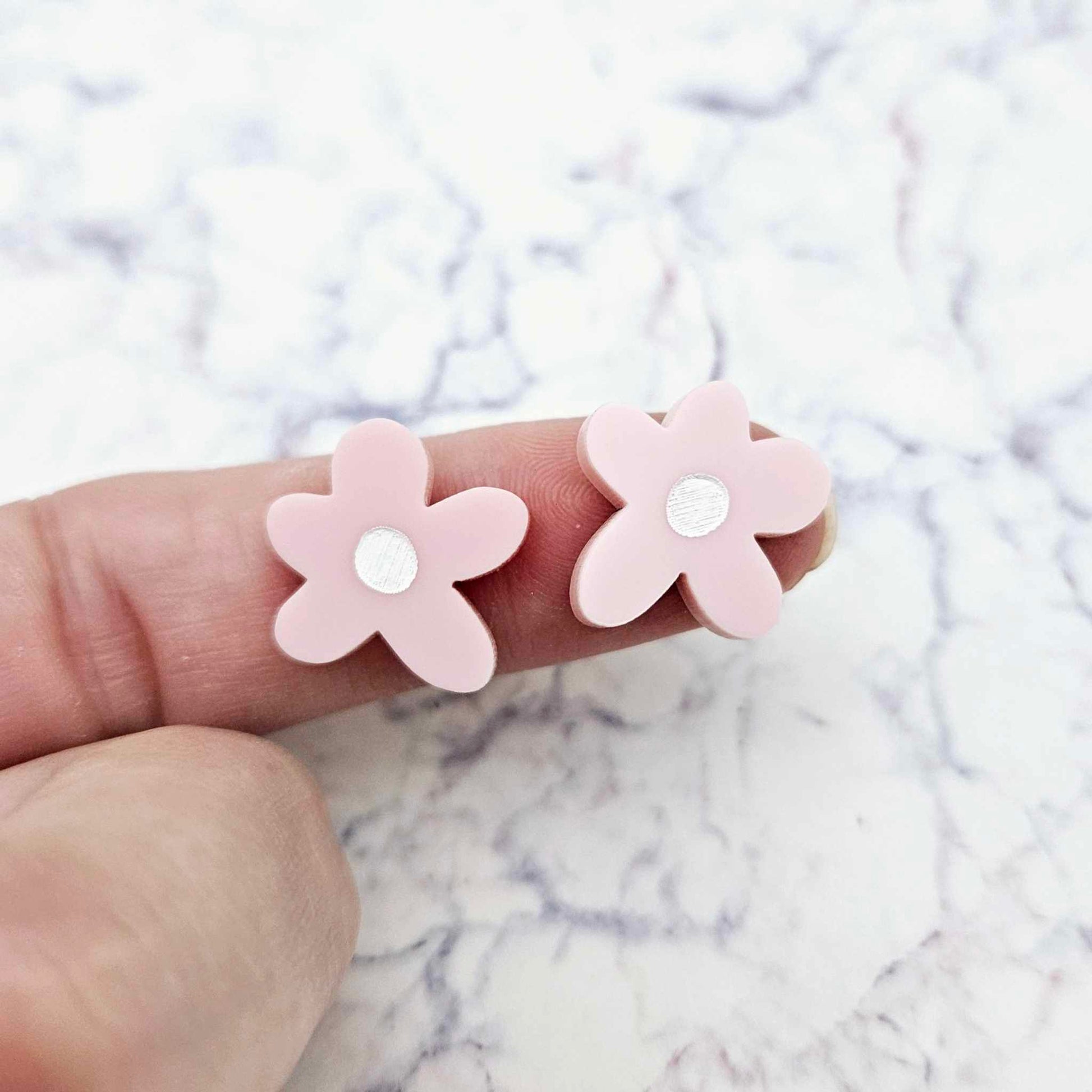 Two 16mm dusty pale pink organic flower stud blanks with engraved centre paint filled white, shown on a finger for size reference