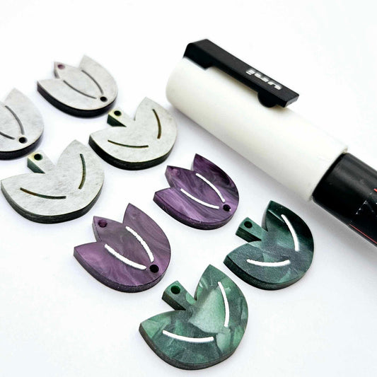 Two-piece tulip acrylic dangle blanks in purple marble and green mineral acrylic, paint filled white on one pair with remaining pair unfilled, shown with a white Posca paint pen