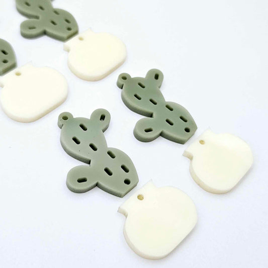 Two-piece acrylic cactus dangle blanks in olive green and cream, shown unassembled with cactus top and pot bottom pieces laid flat