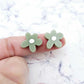 Two 16mm olive green organic flower stud blanks with engraved centre paint filled white, shown on a finger for size reference
