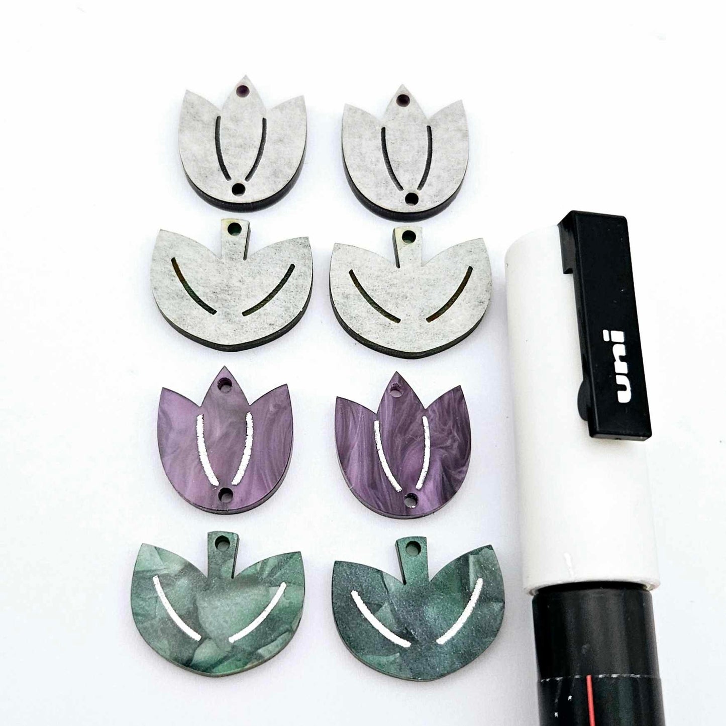 Two-piece tulip acrylic dangle blanks in purple marble and green mineral acrylic, paint filled white on one pair with remaining pair unfilled, shown with a white Posca paint pen
