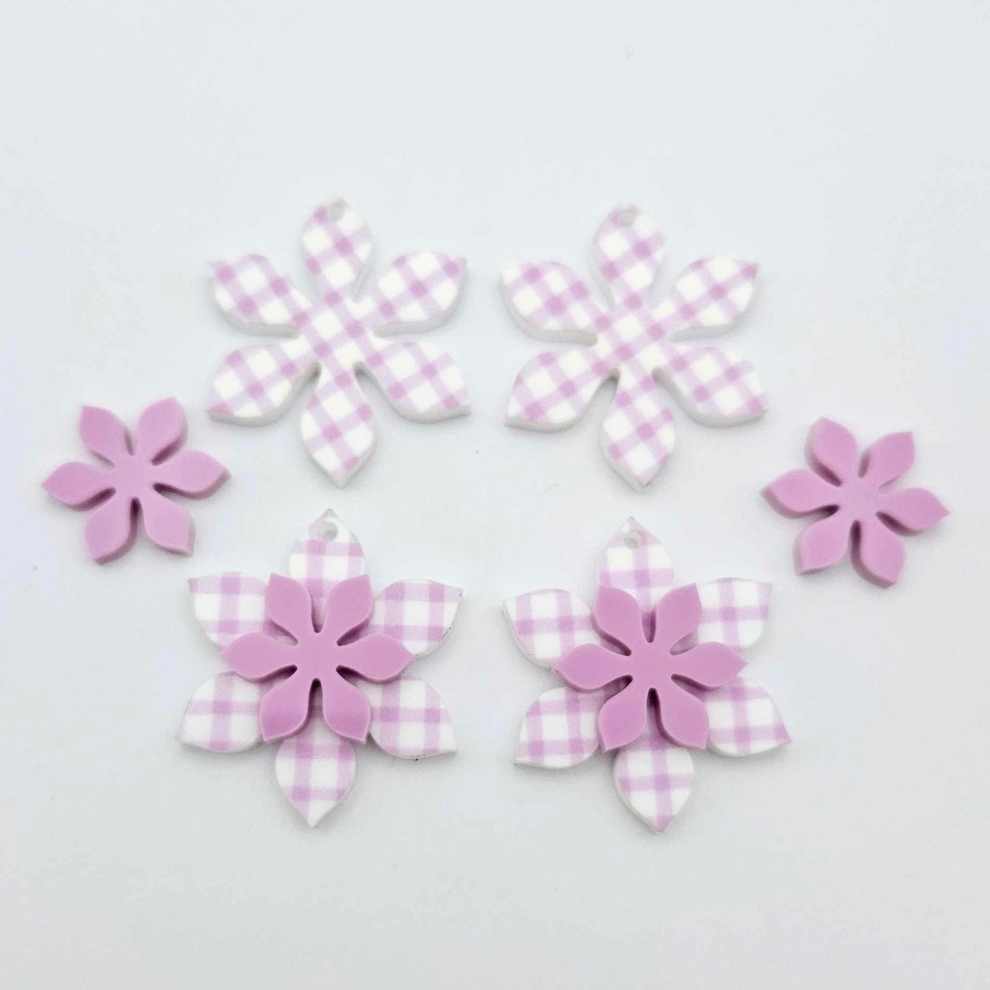 Purple gingham UV print and sour grape acrylic two layer flower dangle blanks shown laying flat, with some flowers stacked to show layered effect and others positioned side by side